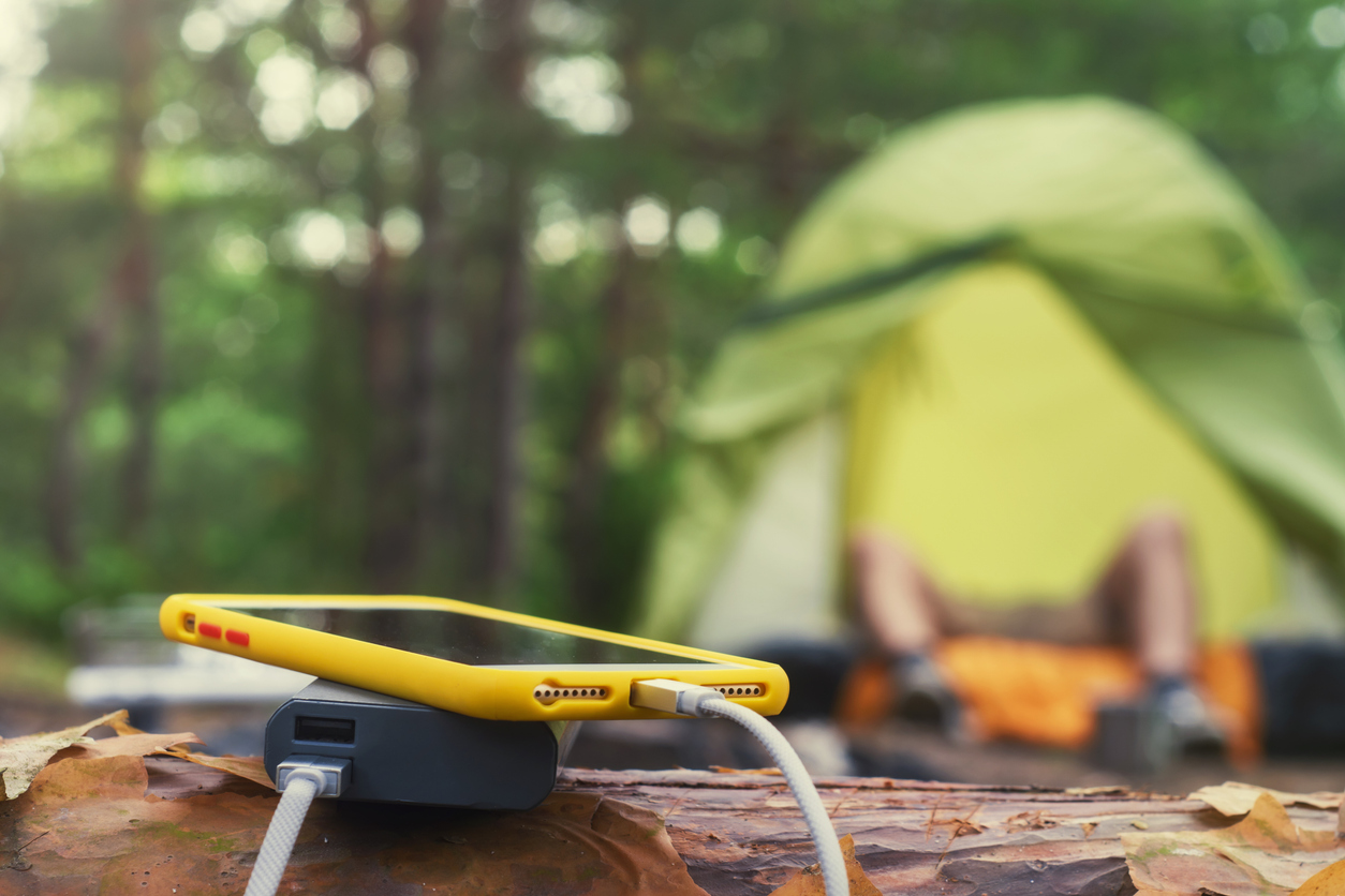 Mòbil endollat a una bateria externa amb el bosc i una tenda de campanya de fons