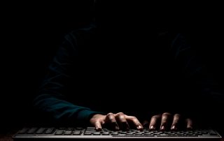Mans sobre un teclat d'ordinador en un ambient fosc
