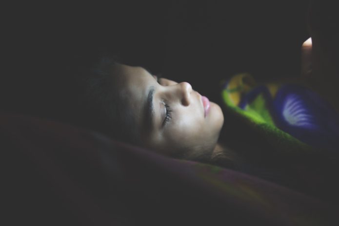 Noia fent servir el mòbil al llit, a la nit