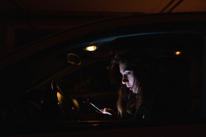 Noia dins d'un cotxe, revisant el seu telèfon mòbil amb preocupació