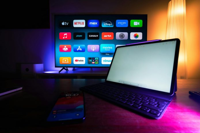 Pantalla amb plataformes de streaming com Netflix, Disney+ i Prime Video en una habitació fosca, representant la competició per l’atenció i el consum digital de continguts.